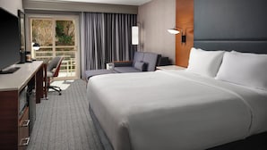 Habitación de hotel con una cama grande, un escritorio, una silla, un televisor y un ventanal con cortinas.