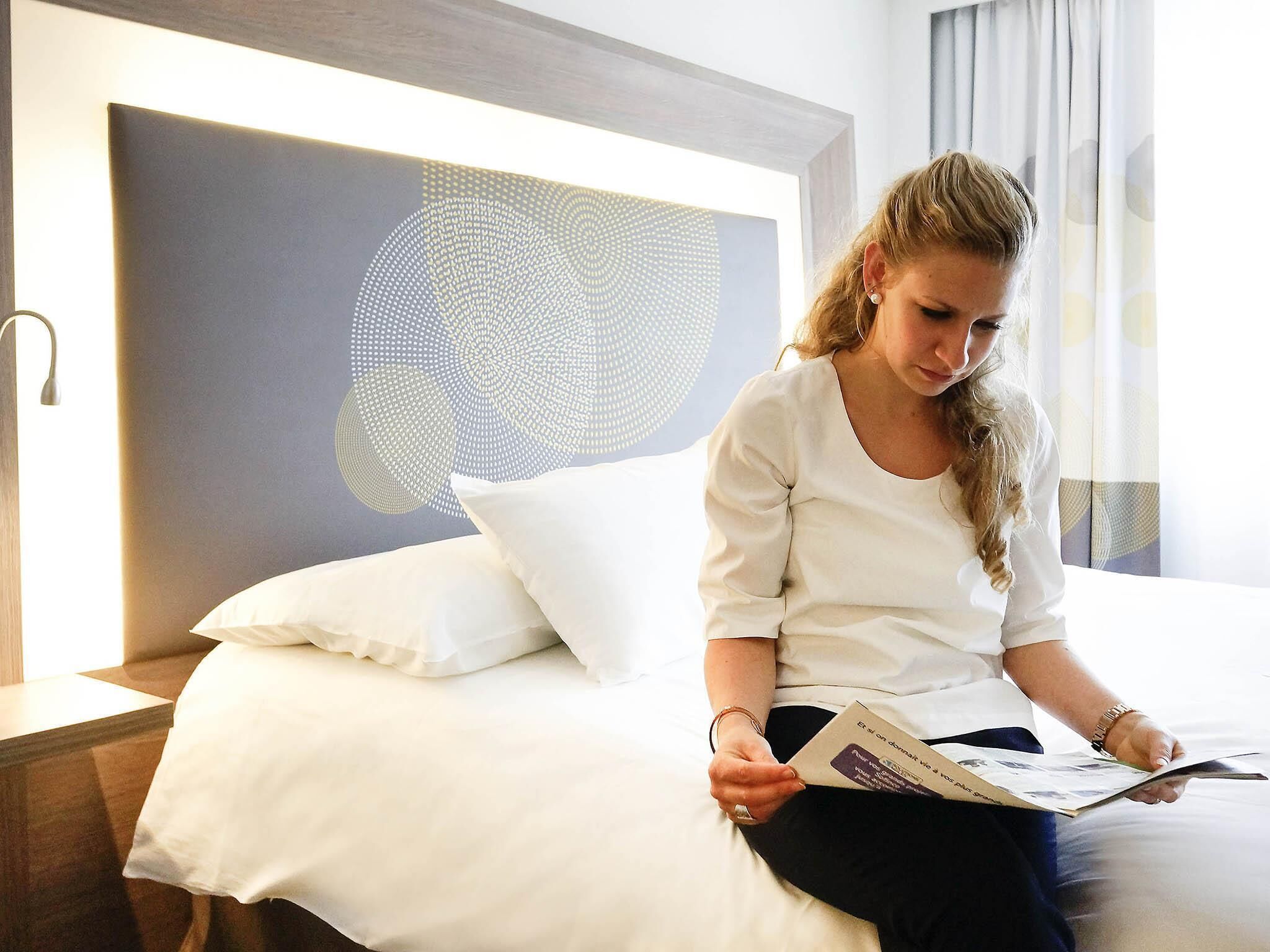 A person sitting on a bed in a hotel room with a modern headboard and a large abstract wall art piece.