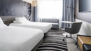 A modern hotel room with two beds, a sofa, a desk, and a TV. - Novotel Paris Saclay (Saclay)