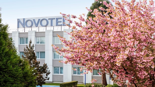 A Novotel hotel building with a sign, surrounded by blooming cherry blossom trees. - Novotel Paris Saclay (Saclay)