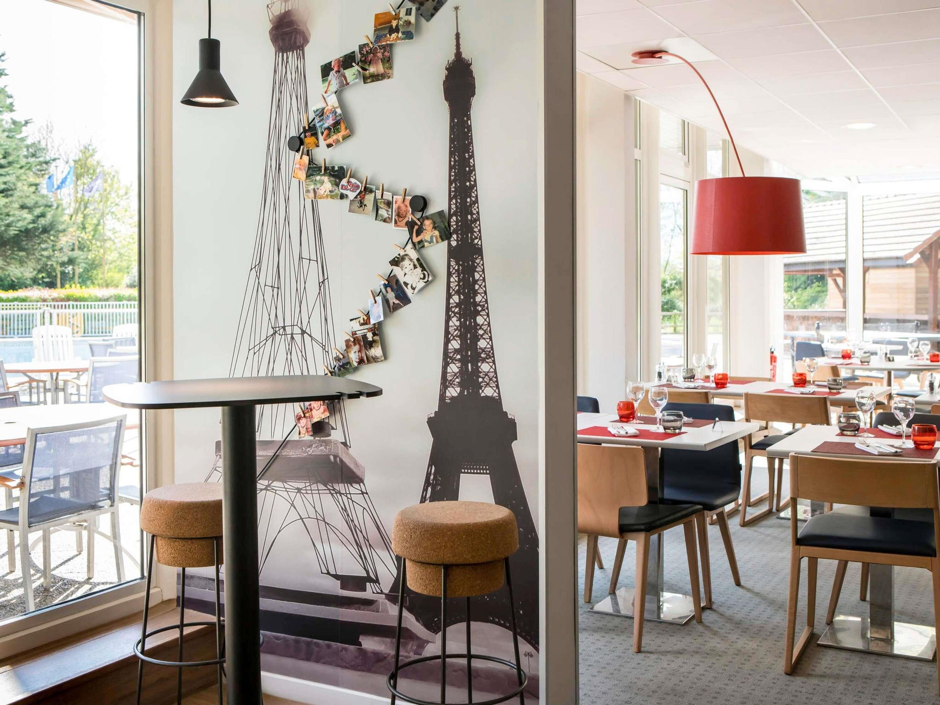 Un comedor con mesas y sillas, una pared decorada con la Torre Eiffel, y una lámpara colgante.