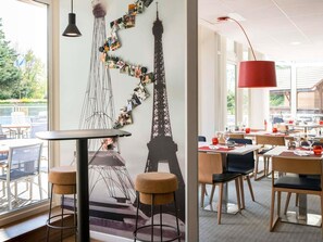 Un comedor con mesas y sillas, una pared decorada con la Torre Eiffel, y una lámpara colgante.
