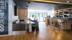 A restaurant with a bar area, seating arrangements, and a view through large windows. - Novotel Paris Saclay (Saclay)