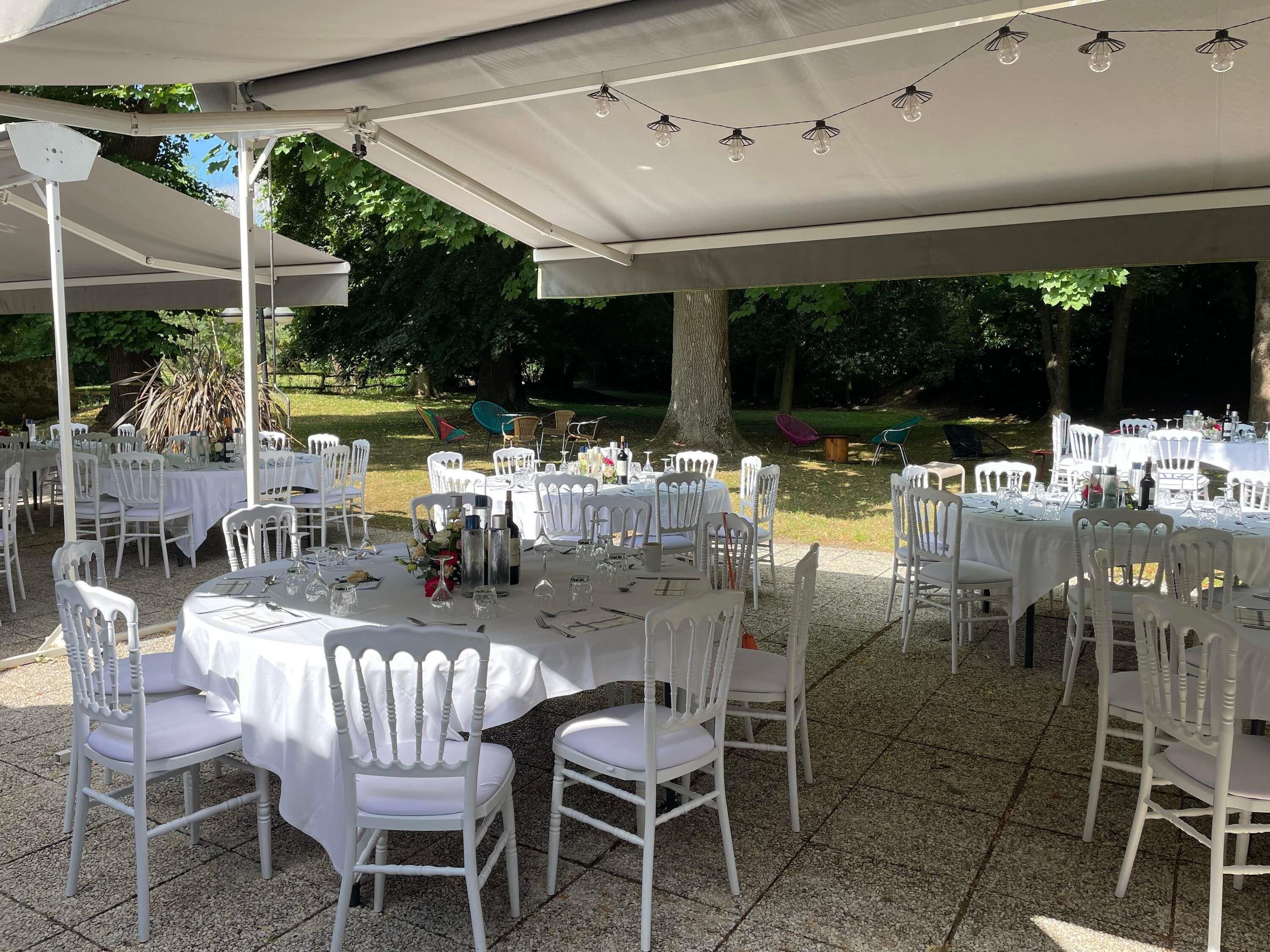 An outdoor event space with round tables, white chairs, and string lights.