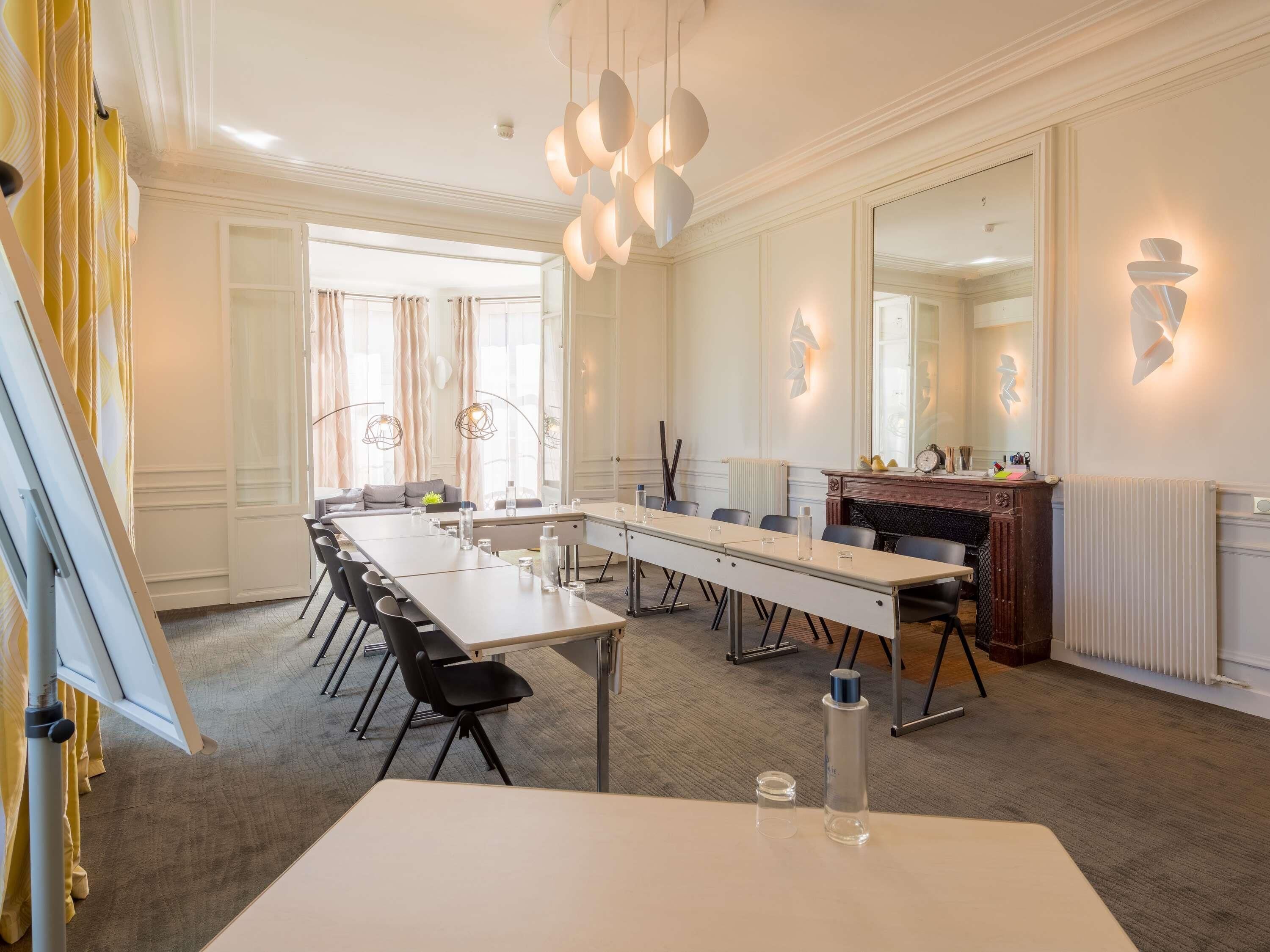 Een vergaderruimte met een lange tafel, stoelen, een open haard en een grote spiegel.