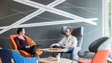 Un intérieur moderne avec deux personnes assises autour d’une table ronde, entourées de chaises aux couleurs vives.
