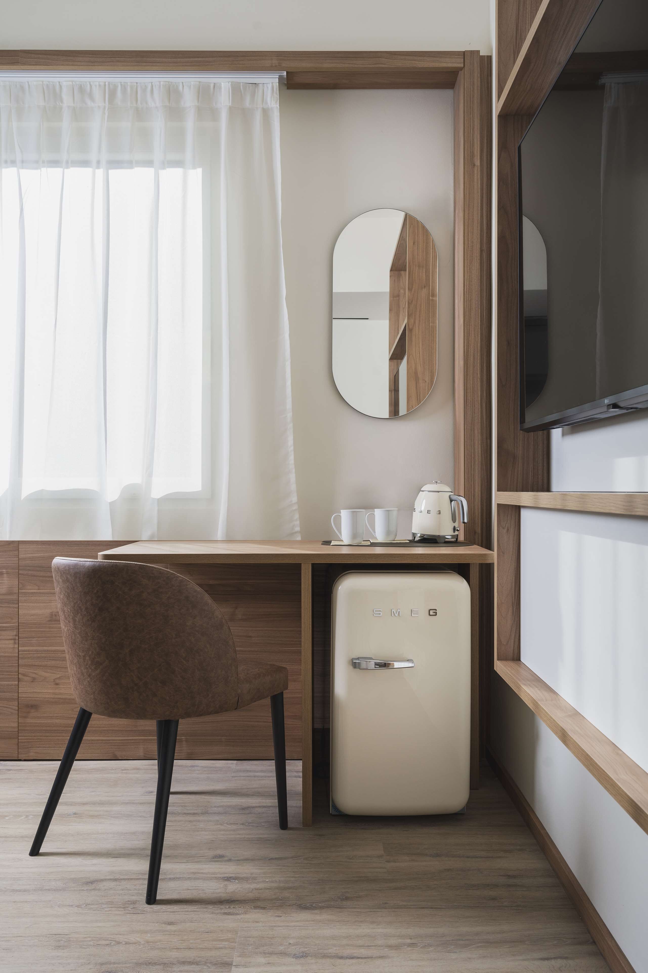 Une chambre d’hôtel de taille réduite, dotée d’un bureau en bois, d’un petit réfrigérateur, d’une chaise, d’une machine à café et d’un téléviseur.