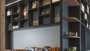 A modern bar area with a counter displaying various snacks and drinks, accompanied by stools and shelves with decorative items. - Hilton Garden Inn Padova City Centre (Padova)