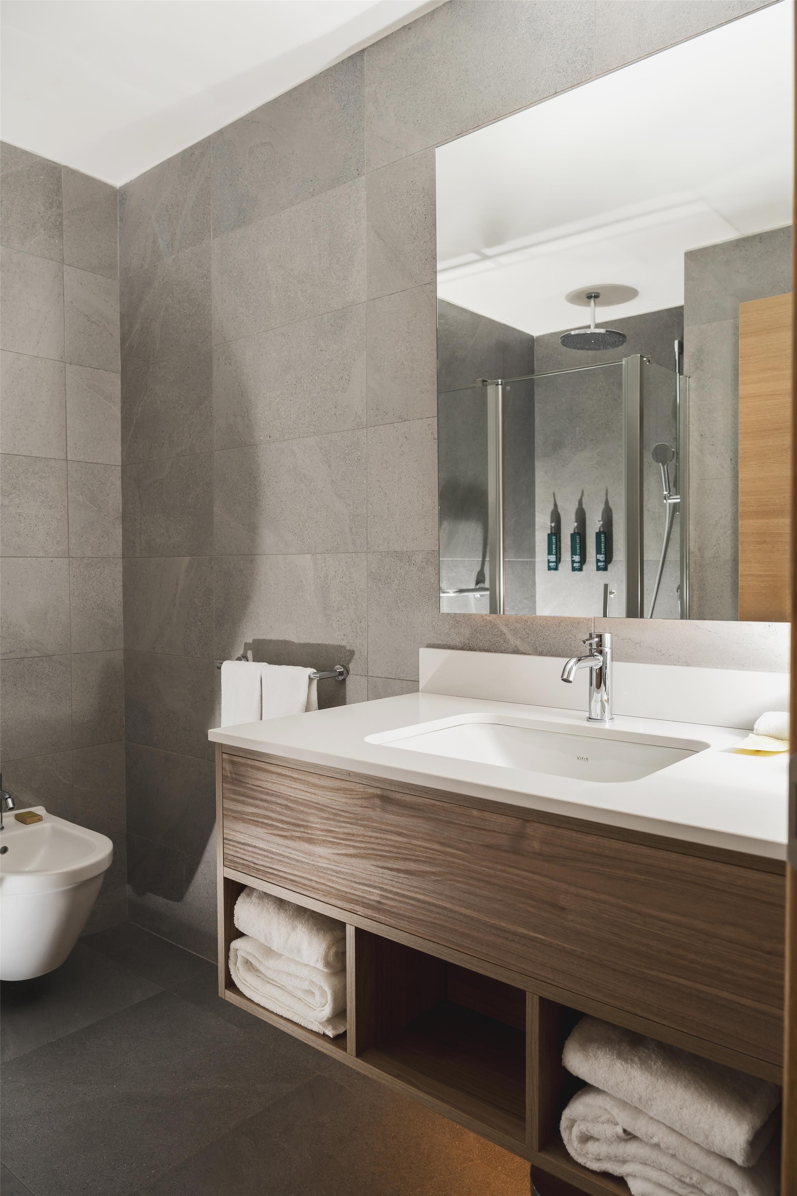 Et stilfuldt badeværelse med et dobbelt vaskeskrin, et spejl og en bruseniche.
