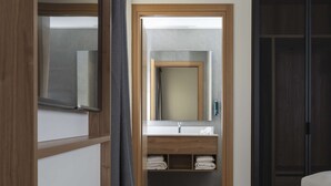 A hotel room with a wooden floor, a large mirror above the sink, a dark wardrobe, and a bed. - Hilton Garden Inn Padova City Centre (Padova)