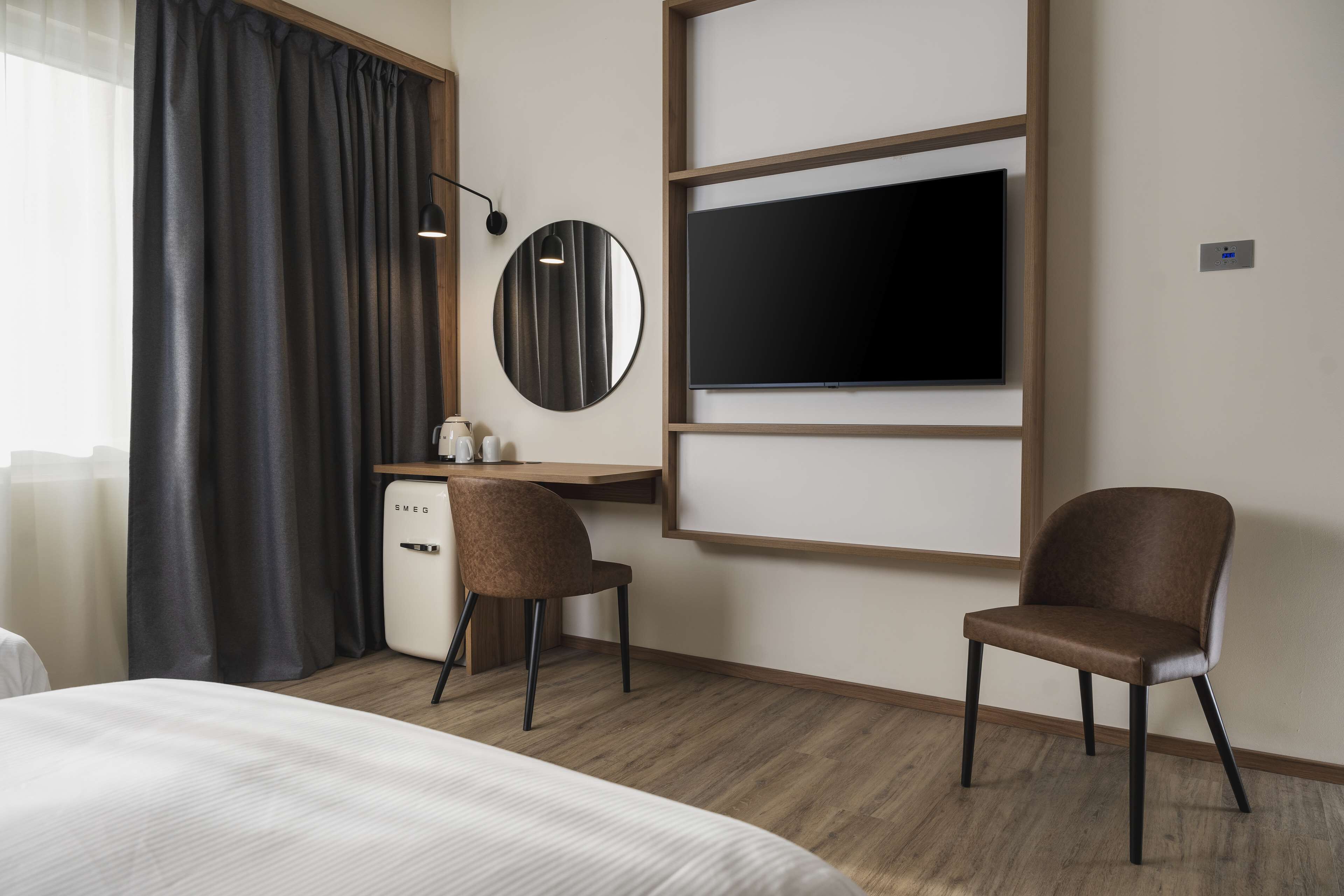 A hotel room with a bed, a desk with a chair, a TV, and a minibar.