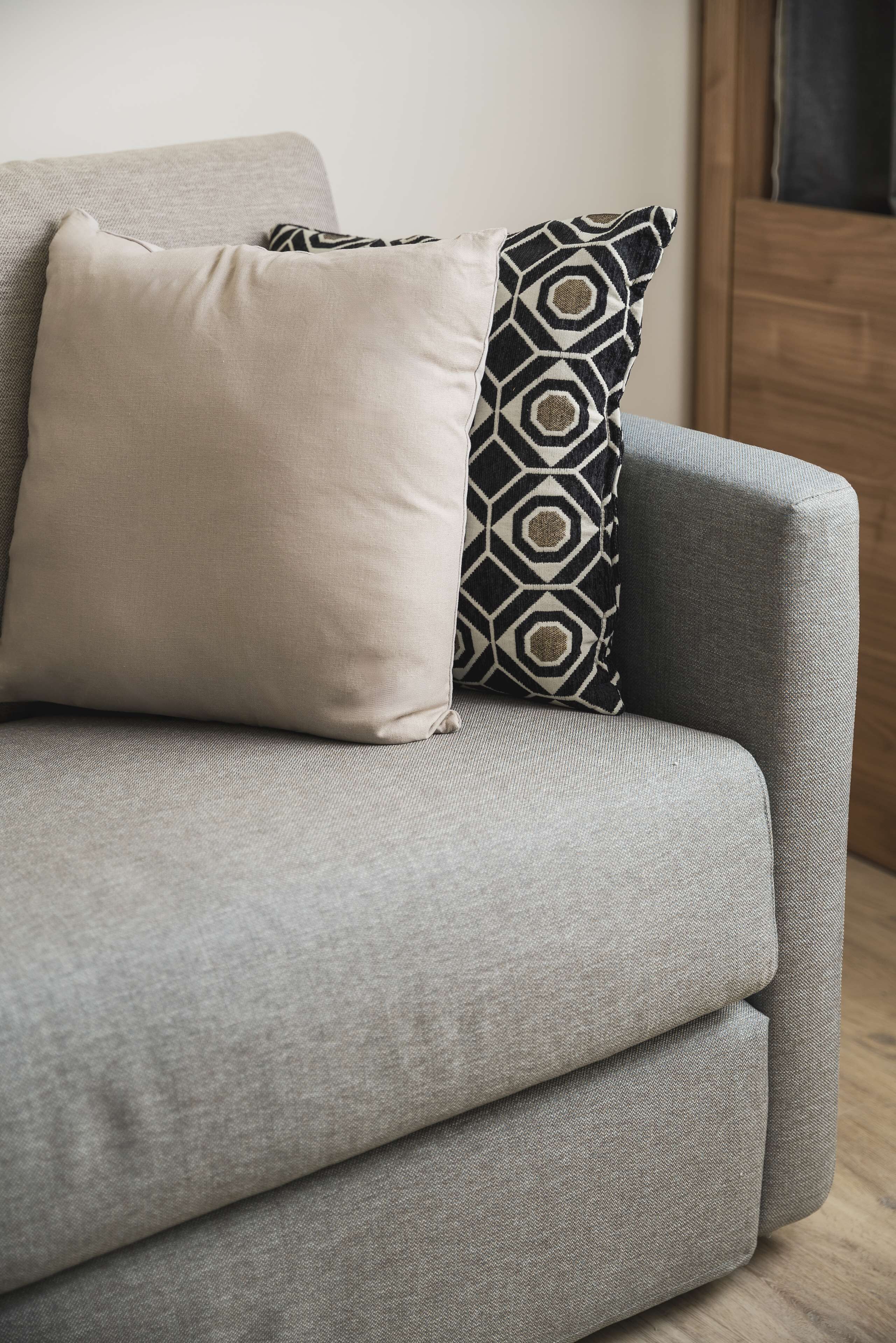 Un sofá gris con dos almohadas, una lisa y otra con un estampado geométrico.