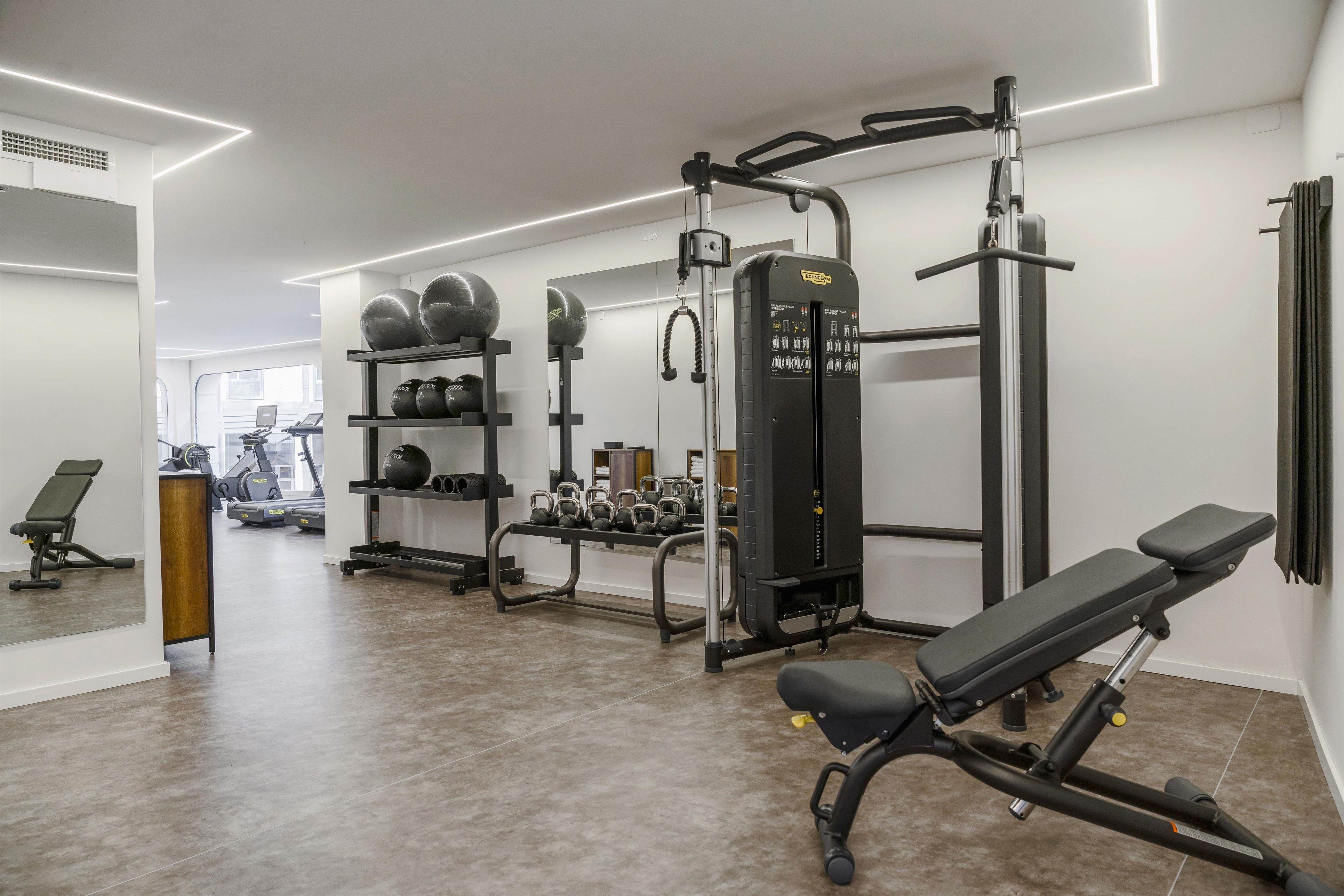 Un gimnasio con equipo de ejercicio, una banca y un espejo.