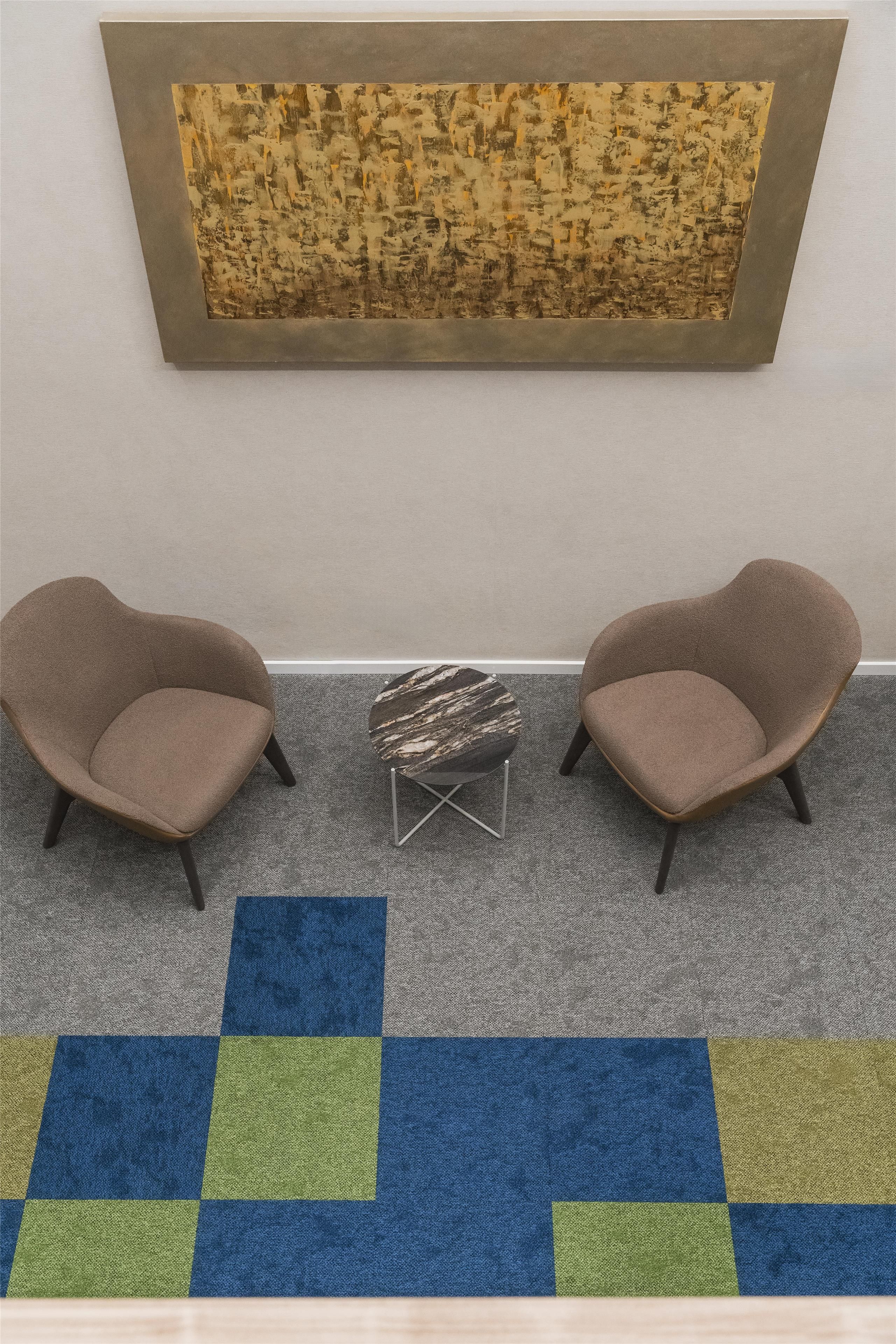 Ein Zimmer mit zwei Sesseln, einem kleinen Couchtisch und einem großen, abstrakten Gemälde an der Wand.