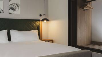A hotel room with a bed, a round table, a wall-mounted lamp, and artwork.