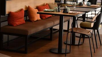 Un café moderno con un banco de madera, sillas de metal negro y una mesa dispuesta con una tetera, tazas y un plato.