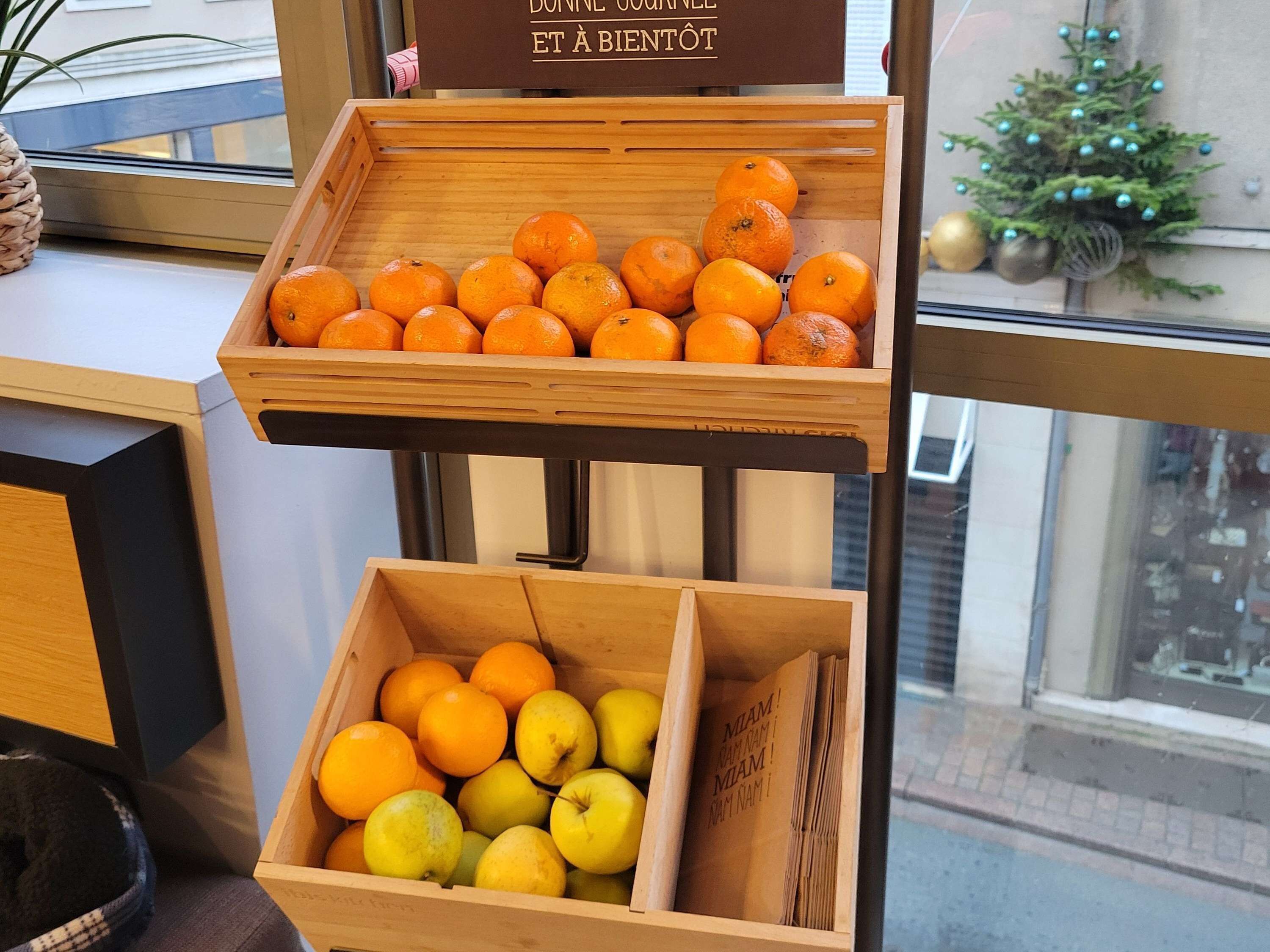Una exhibición de madera con naranjas y manzanas, y un cartel encima.
