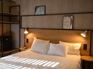 Ein Hotelzimmer mit einem Holzkopfteil, zwei Nachttischlampen, einem Bett mit weißen Bettwäsche und einem kleinen Tisch mit einer Fernbedienung.