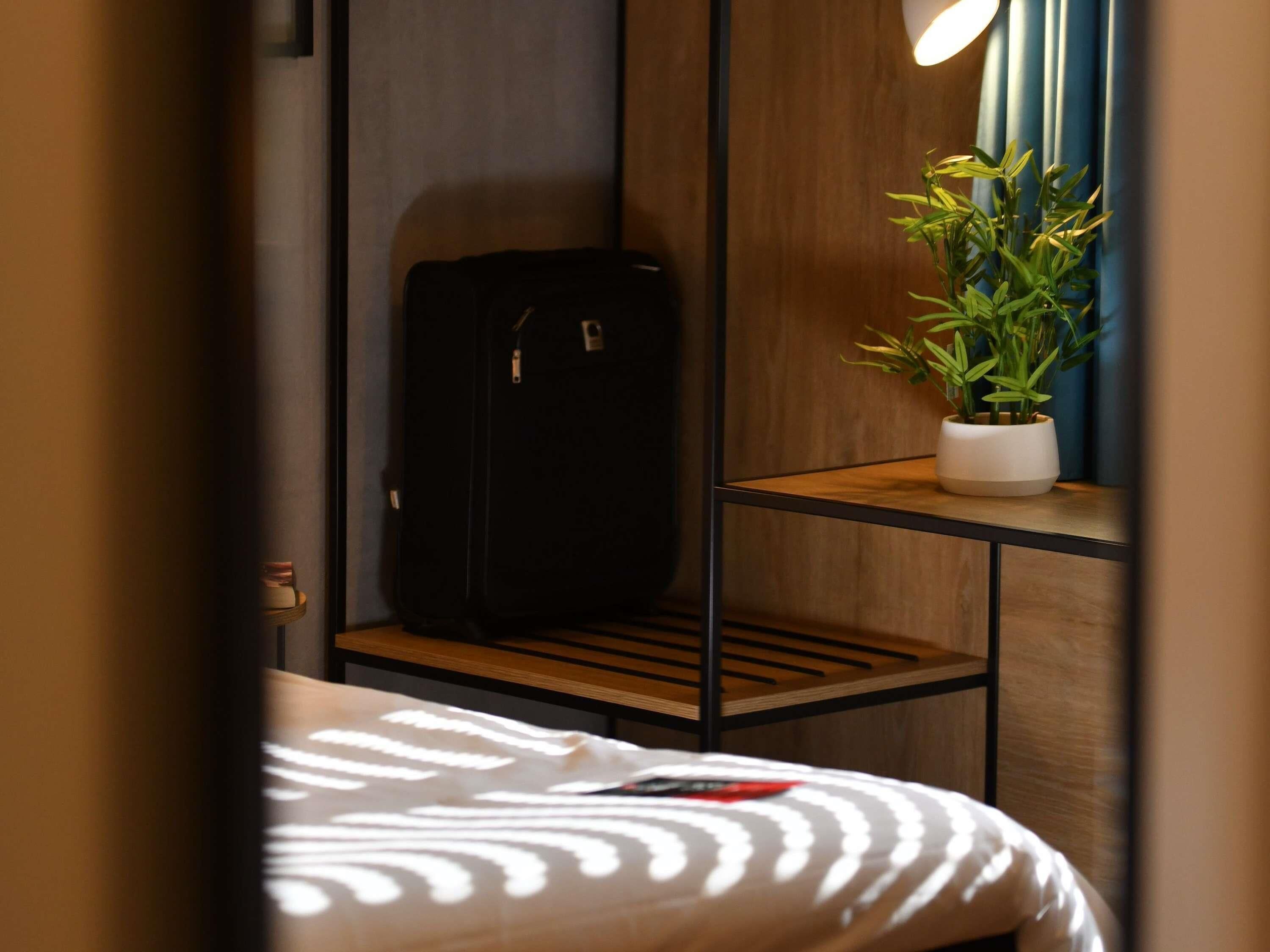 Een hotelkamer met een bed, een klein bureau met een bloempot en een koffer.
