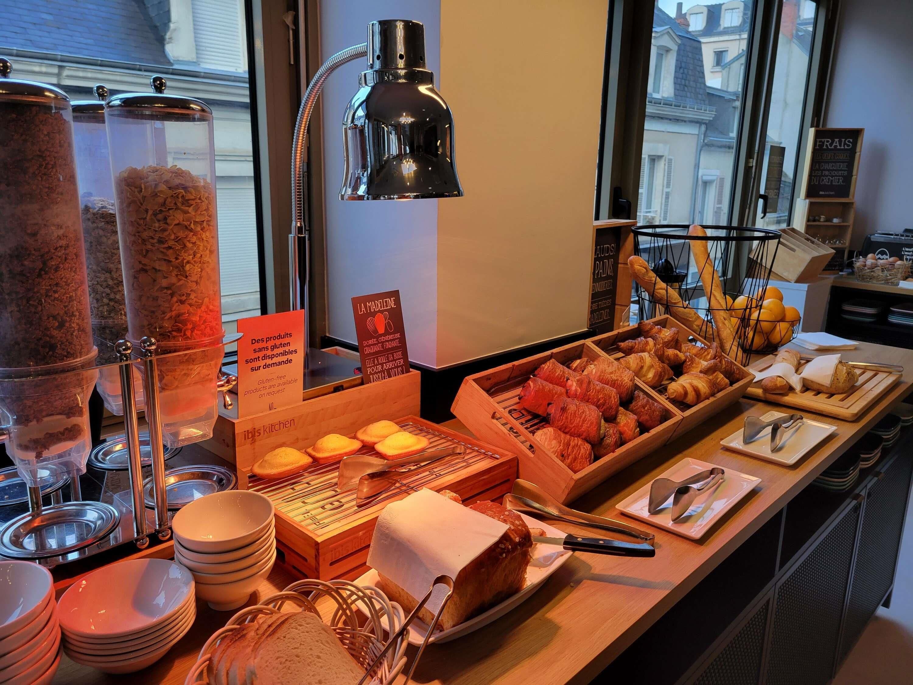 A breakfast buffet with gluten-free options, bread, pastries, and utensils.