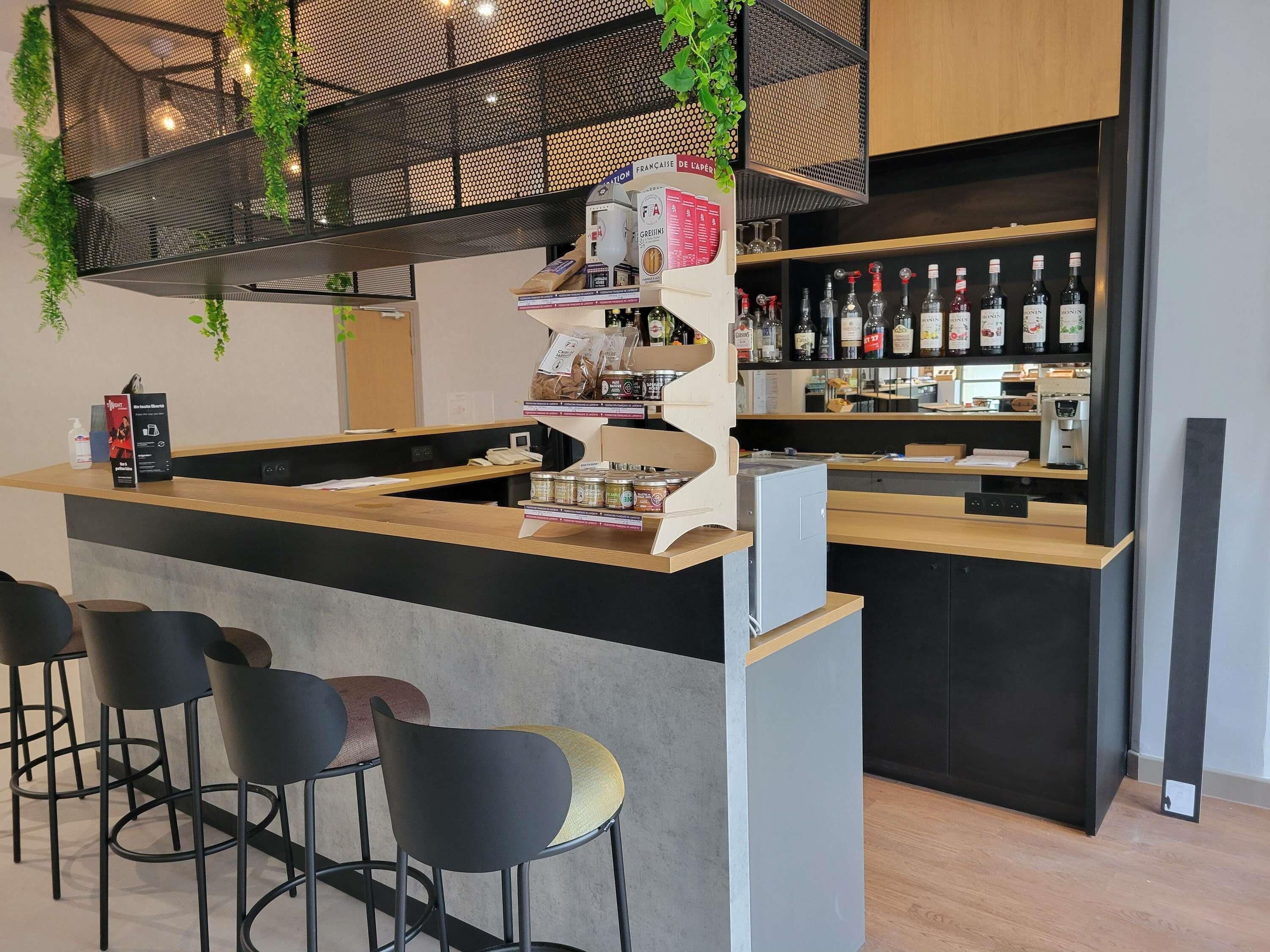Un espace bar moderne, doté d’un comptoir, de tabourets et d’étagères remplies de bouteilles.