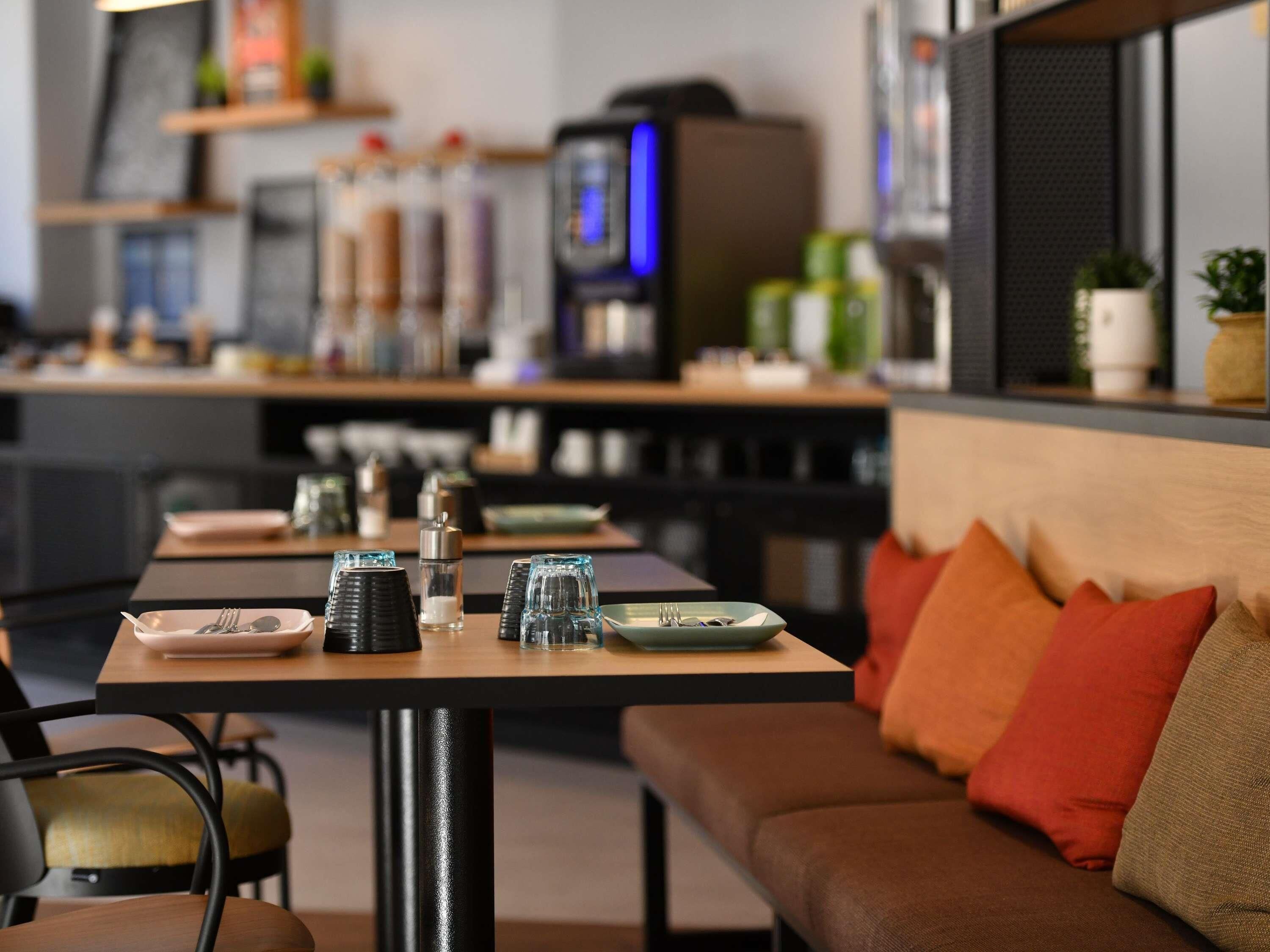 A modern dining area with tables set for two, equipped with cutlery and glasses.