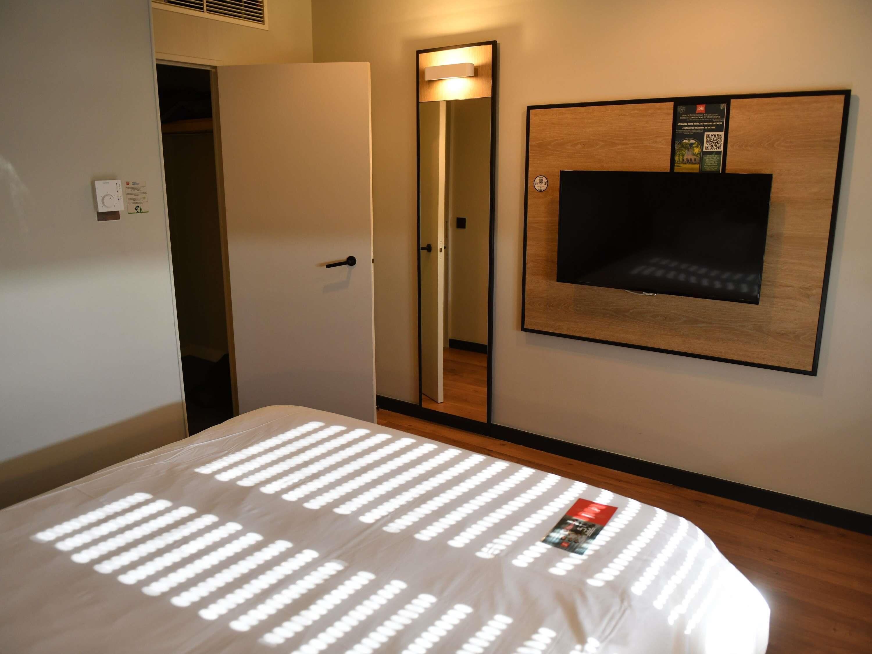 Una habitación de hotel con una cama, un televisor montado en la pared, una puerta y un espejo.