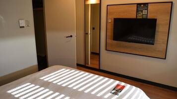 Una habitación de hotel con una cama, un televisor montado en la pared, una puerta y un espejo.