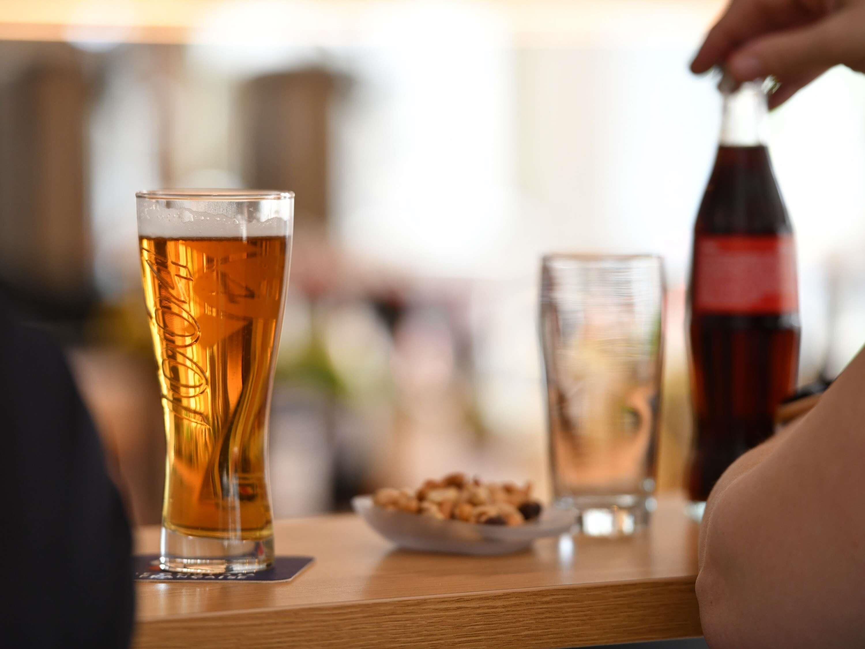 Un verre de bière sur une table en bois, avec une bouteille de soda et une assiette de collations.