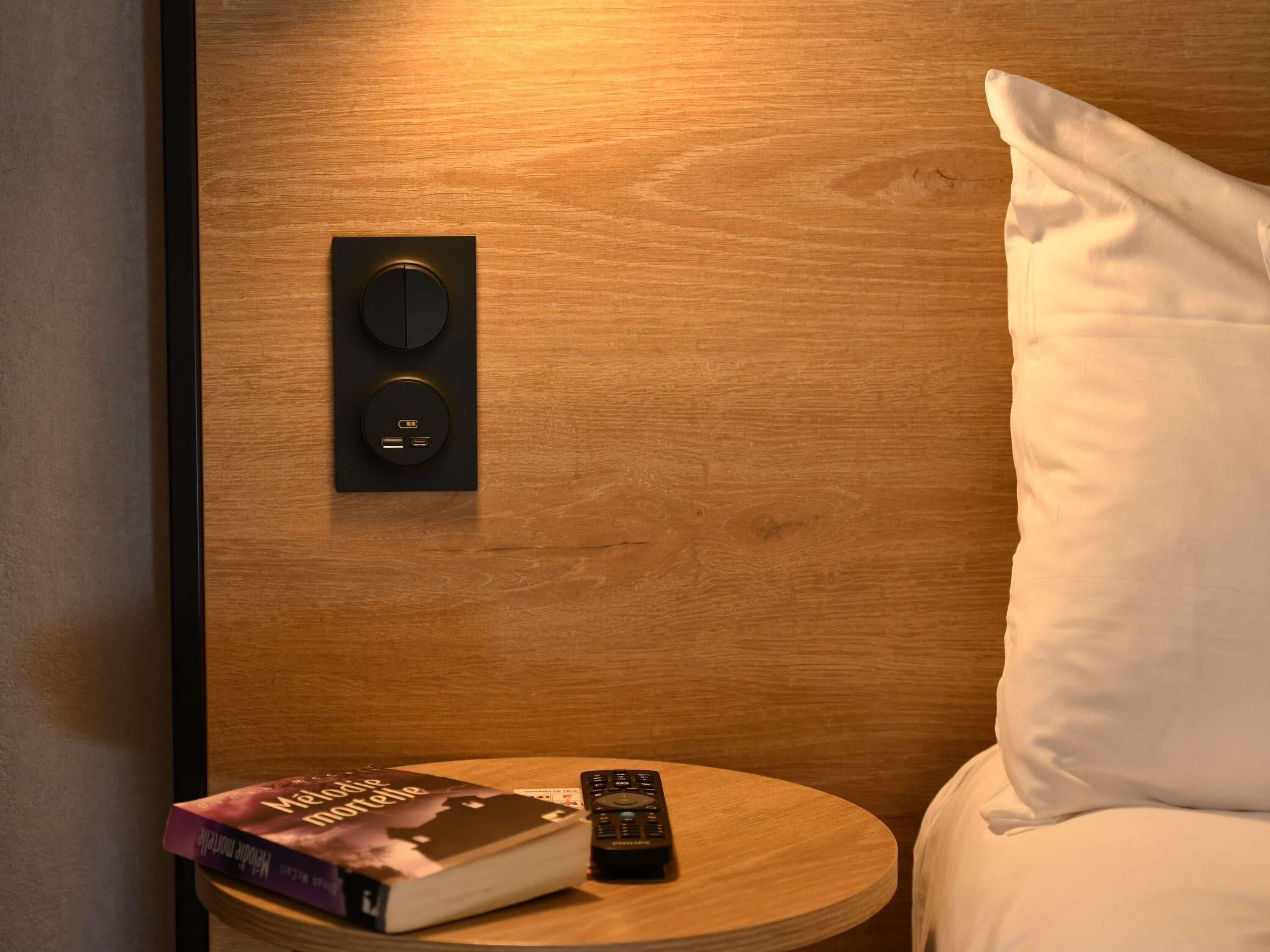 A hotel room with a wooden wall panel, a remote control, a book, and a pillow.