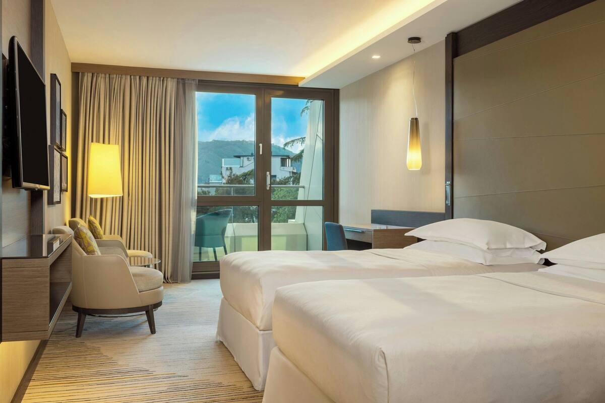 A hotel room with two beds, a desk, a chair, and a TV.