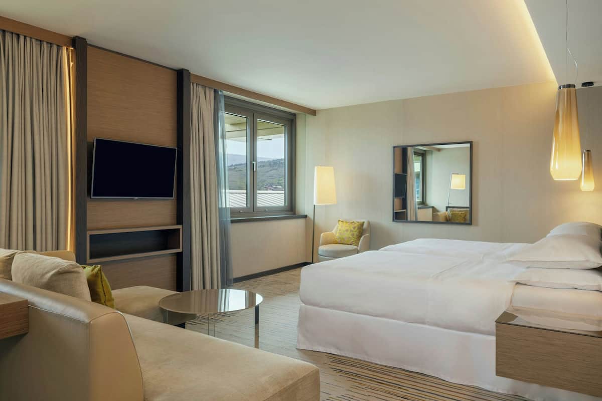 A hotel room with a bed, a sofa, a TV, a lamp, and a window with curtains.