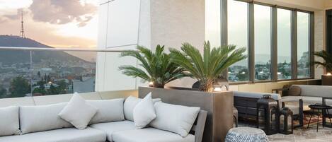 A modern living room with a sofa, a coffee table, and a fireplace. There are large windows offering a city view.