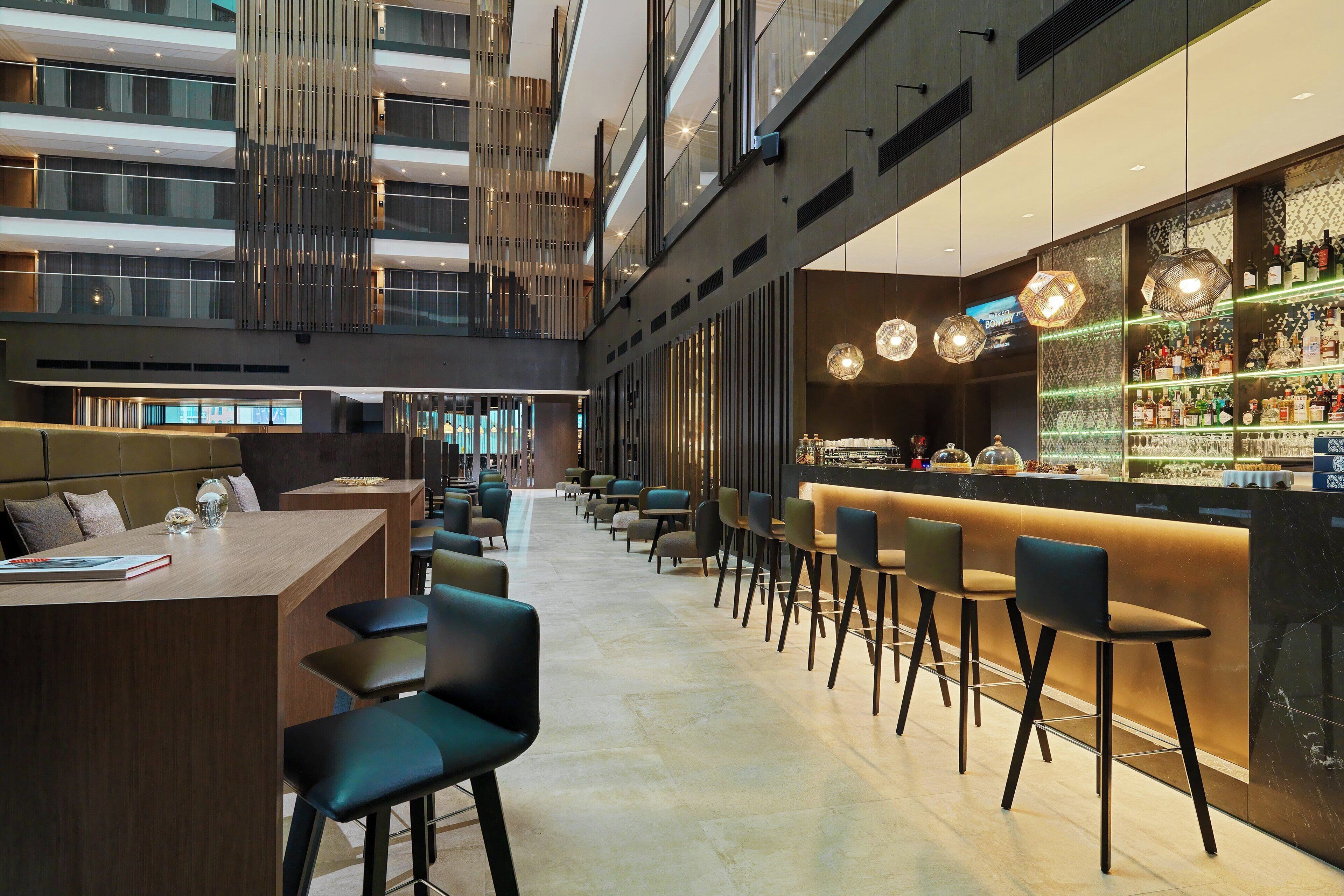 Een moderne bar met een lange toonbank, diverse barkrukken en een goed gevulde bar.