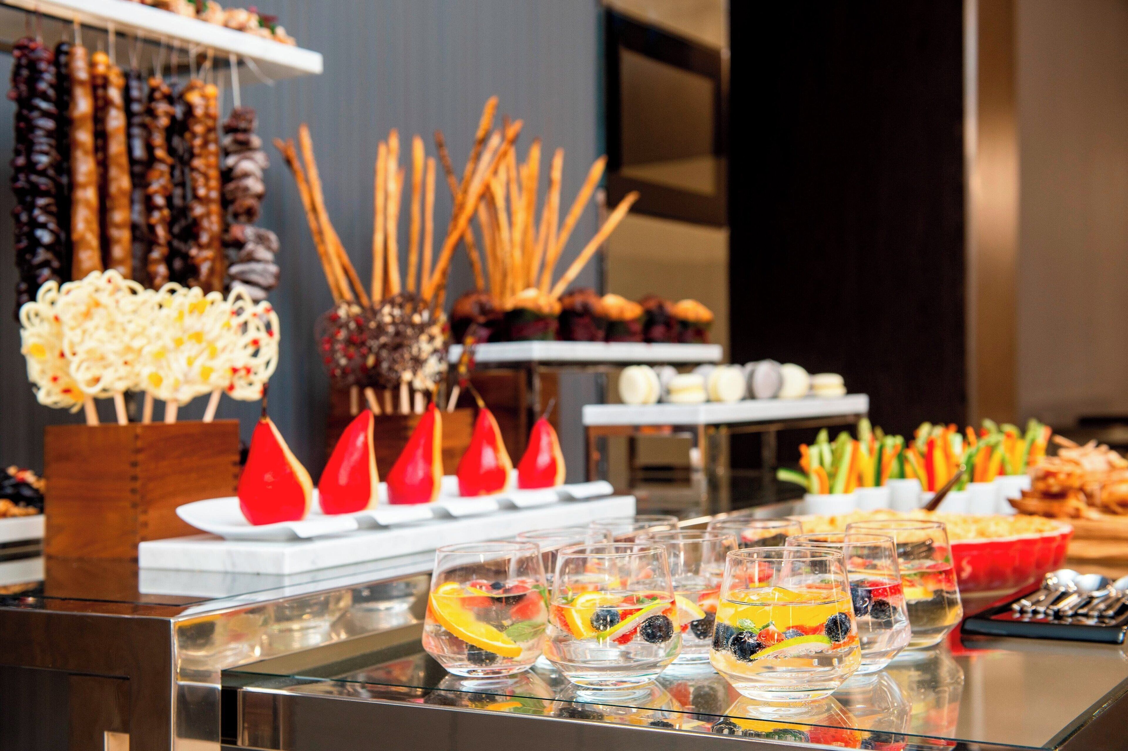 Un buffet proposant une variété de plats, notamment des brochettes, des nouilles et des jus de fruits.