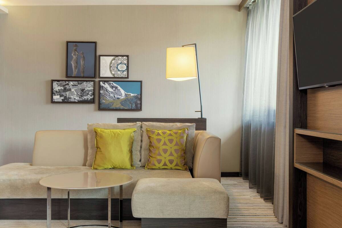 A modern hotel room with a sofa, a small round table, and a flat-screen TV.