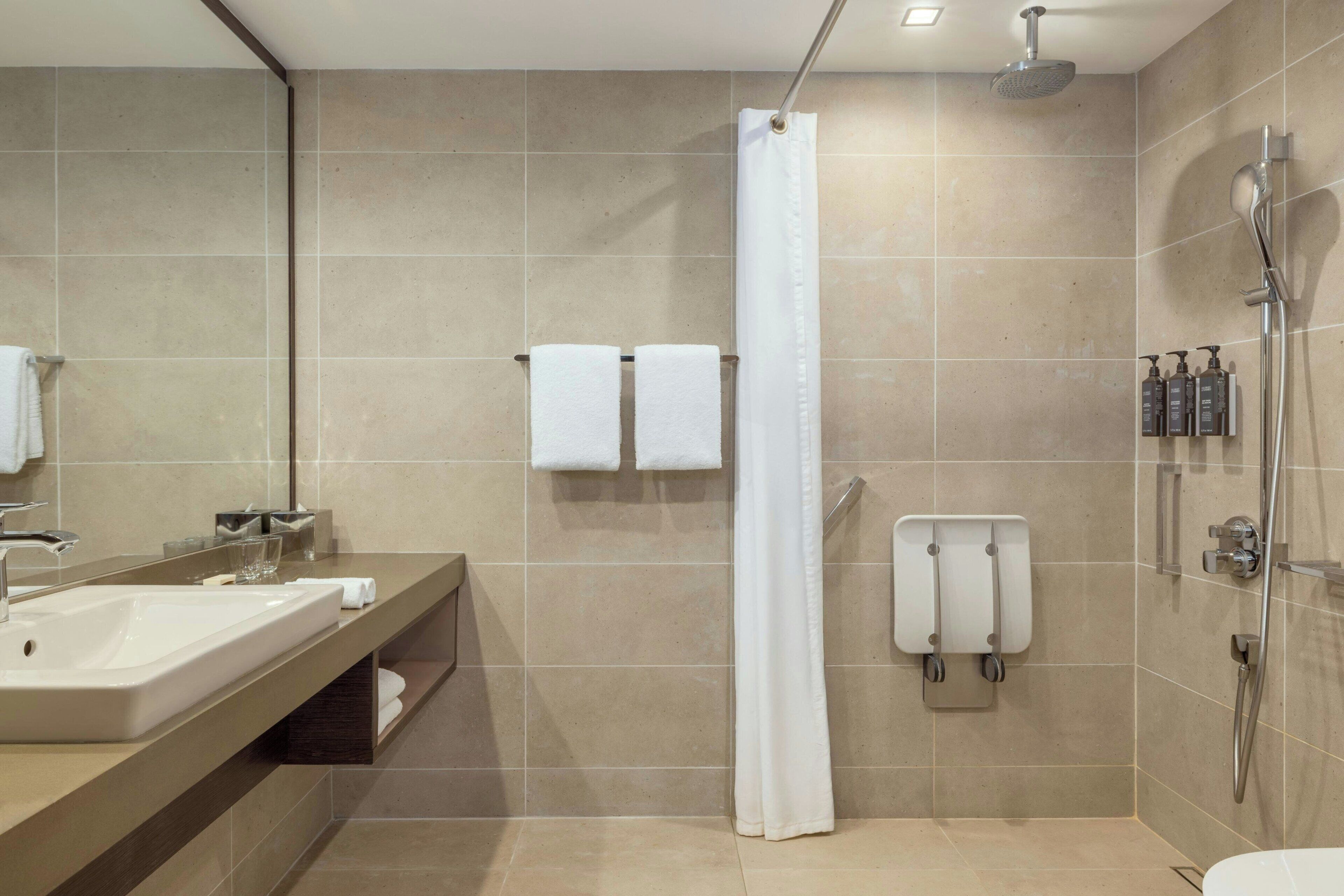 Un baño moderno con un lavamanos grande, dos toallas, una ducha con cabezal de ducha manual y un vaso de agua en la encimera.