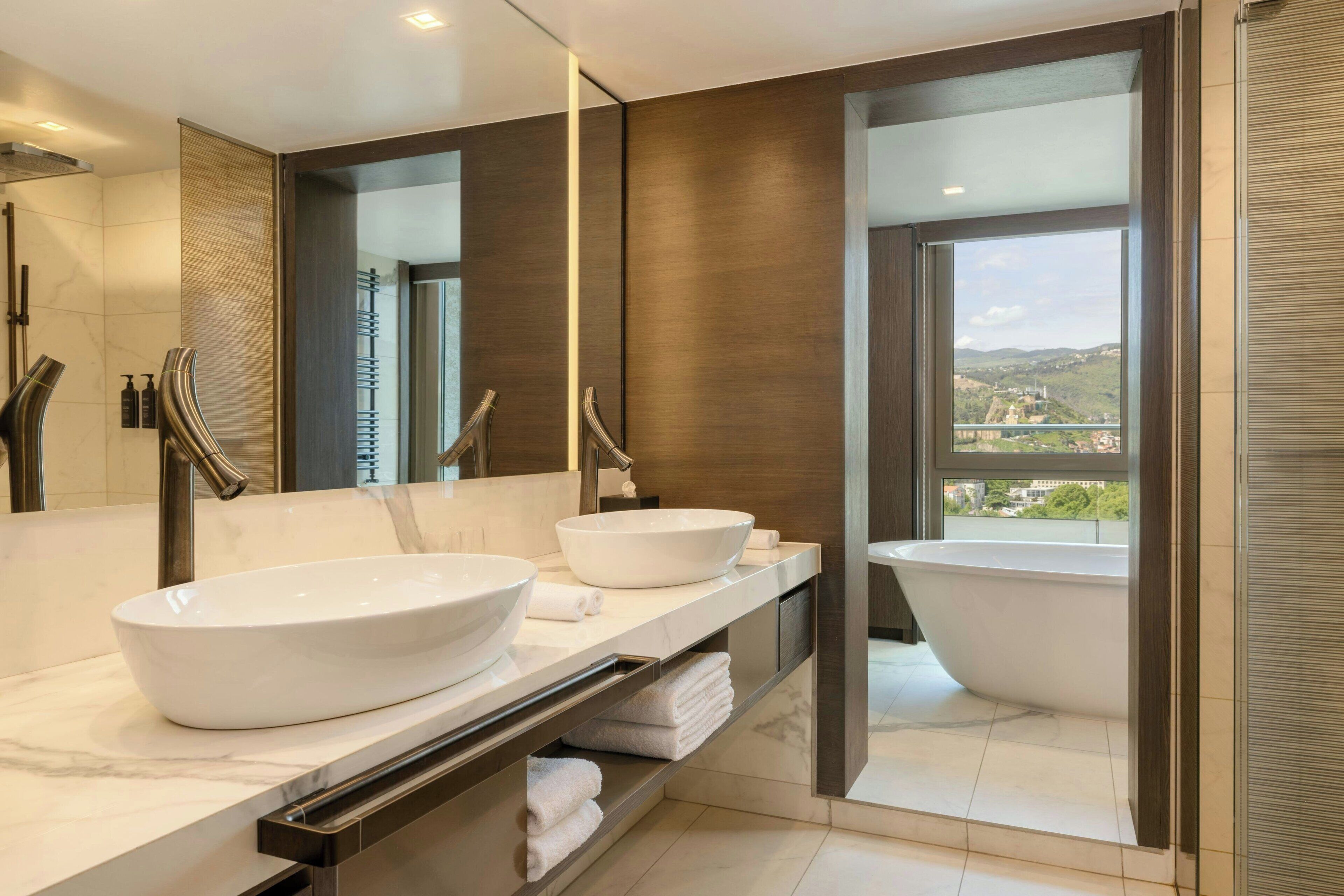 A modern bathroom with two large white sinks, a freestanding bathtub, and a large mirror.