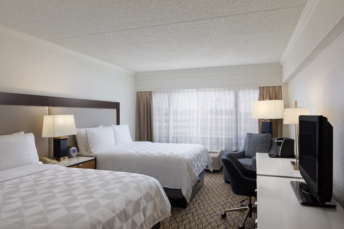 A hotel room with two beds, a desk with a TV, and a chair.