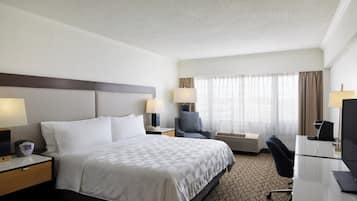 A hotel room with a bed, two bedside tables, a desk with a chair, a television, and a window with curtains.