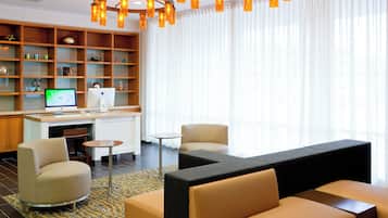 Un moderno vestíbulo de hotel con una zona de estar, un escritorio con computadora y una estantería con objetos decorativos.