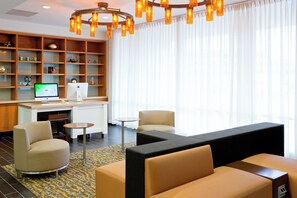 A modern hotel lobby with a seating area, a desk with a computer, and a bookshelf with decorative items. - Holiday Inn Clark - Newark Area by IHG (Clark)