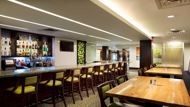 A bar area with a long counter, multiple stools, and a seating area with tables and chairs. - Holiday Inn Clark - Newark Area by IHG (Clark)