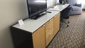 A hotel room with a flat-screen TV on a wooden cabinet, a grey armchair, a desk with a lamp, and a patterned carpet. - Holiday Inn Clark - Newark Area by IHG (Clark)