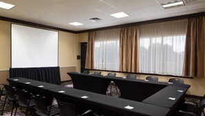 Un salón de conferencias con una larga mesa, sillas, una pantalla de proyector y un amplio ventanal con cortinas.
