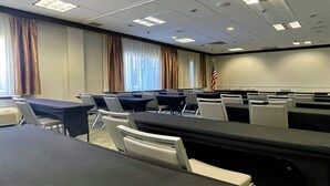 A conference room with multiple tables and chairs, large windows with curtains, and an American flag on the wall. - Holiday Inn Clark - Newark Area by IHG (Clark)