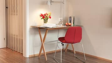 Un espacio de trabajo moderno con un escritorio de madera, una silla roja, una lámpara de escritorio, un jarrón con flores y algunos libros y manzanas.