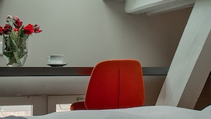 A room with a skylight, a red chair, a bed, and a vase with flowers. - Altstadt Hotel (Zürich)