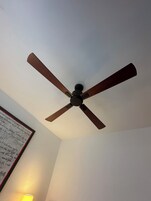 Un ventilador de techo con aspas de madera en una habitación con paredes blancas.