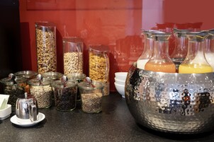 Aamiainen tarjoillaan buffetpöydästä, jossa on erilaisia ruokia lasisissa astioissa ja suuri metallinen kannu.